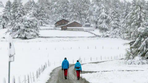 JOHANN GRODER/APA/EXPA/AFP Hikers walk through the snow-covered landscape at the Kalser K?dnitztal valley in Kals am Grossglockner, Tyrol, Austria, on September 13, 2024